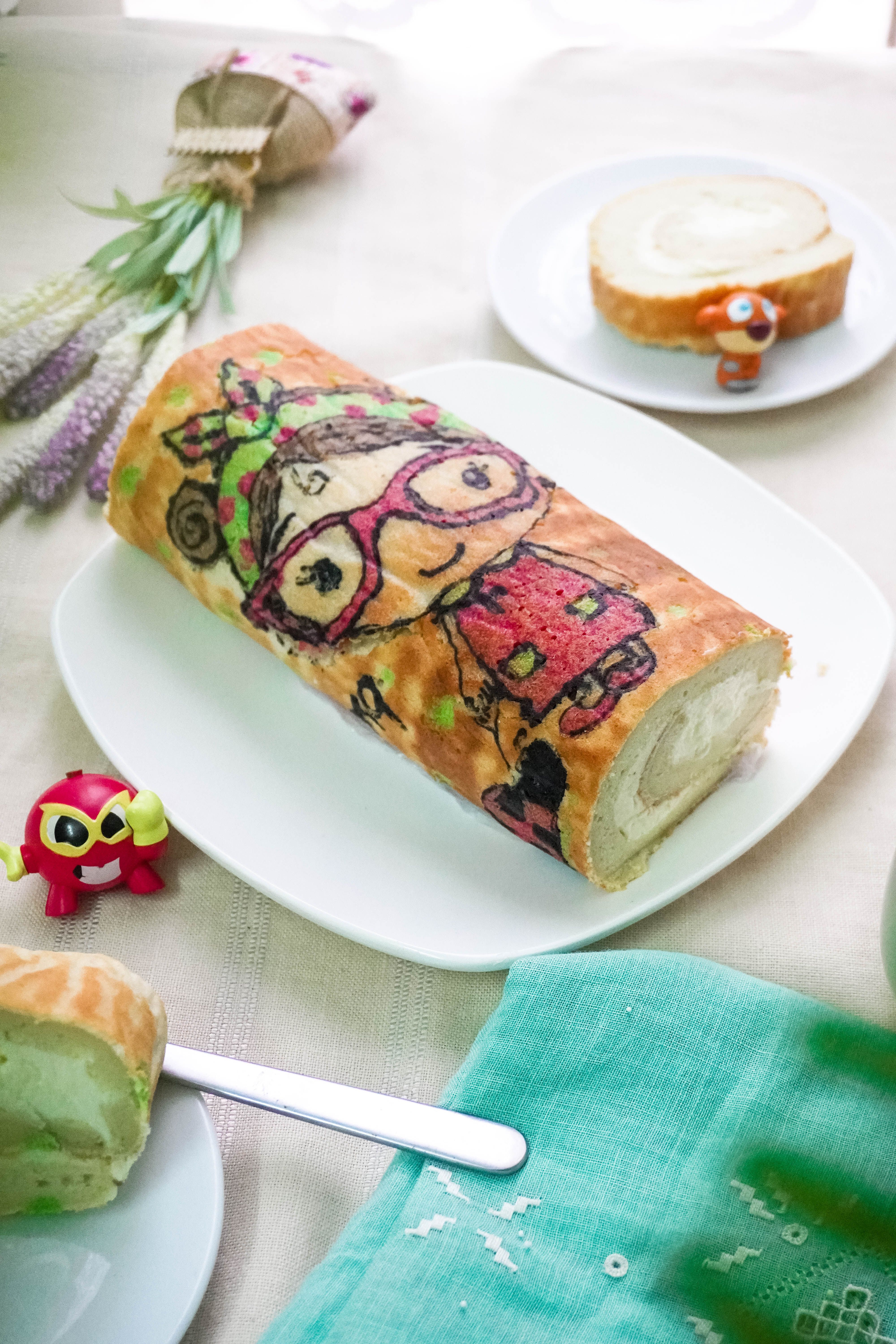 Colorful cartoon-themed Swiss roll cake with decorations on a white plate.