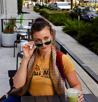 Stylish woman wearing sunglasses enjoys a fresh drink outdoors.