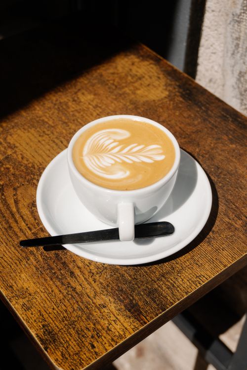 Free Elegant latte with intricate art served outdoors in a Verona café, capturing a warm, relaxed vibe. Stock Photo