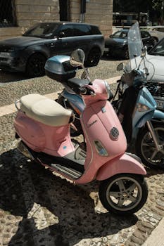 Classic pink Vespa scooter parked on a cobblestone street in Verona, Italy.