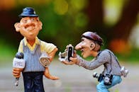 Man Taking Photo Of Man Standing Beside Him Holding Press Microphone Statue