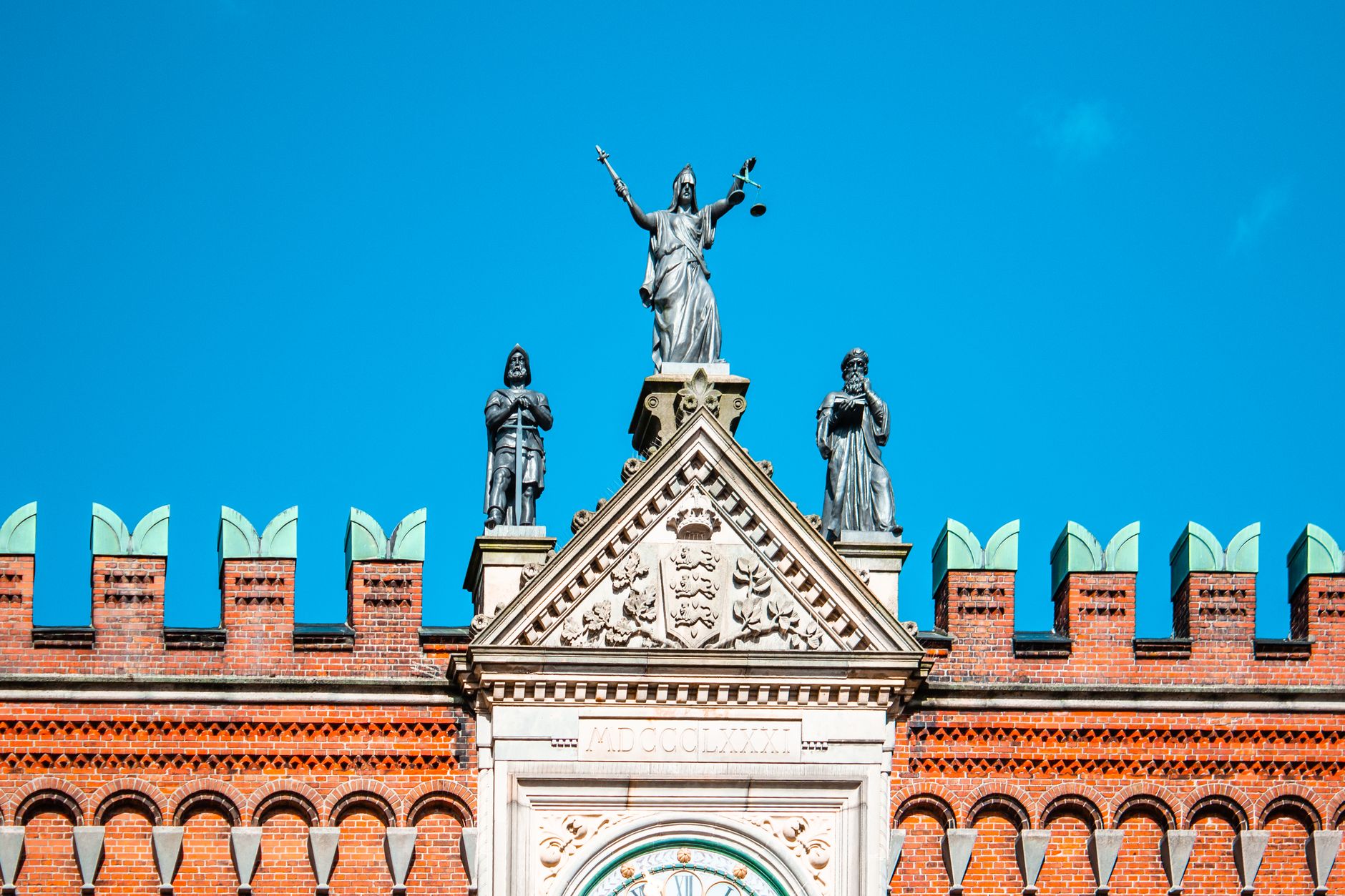Stunning facade of Odense courthouse with Lady Justice statue under clear blue skies.