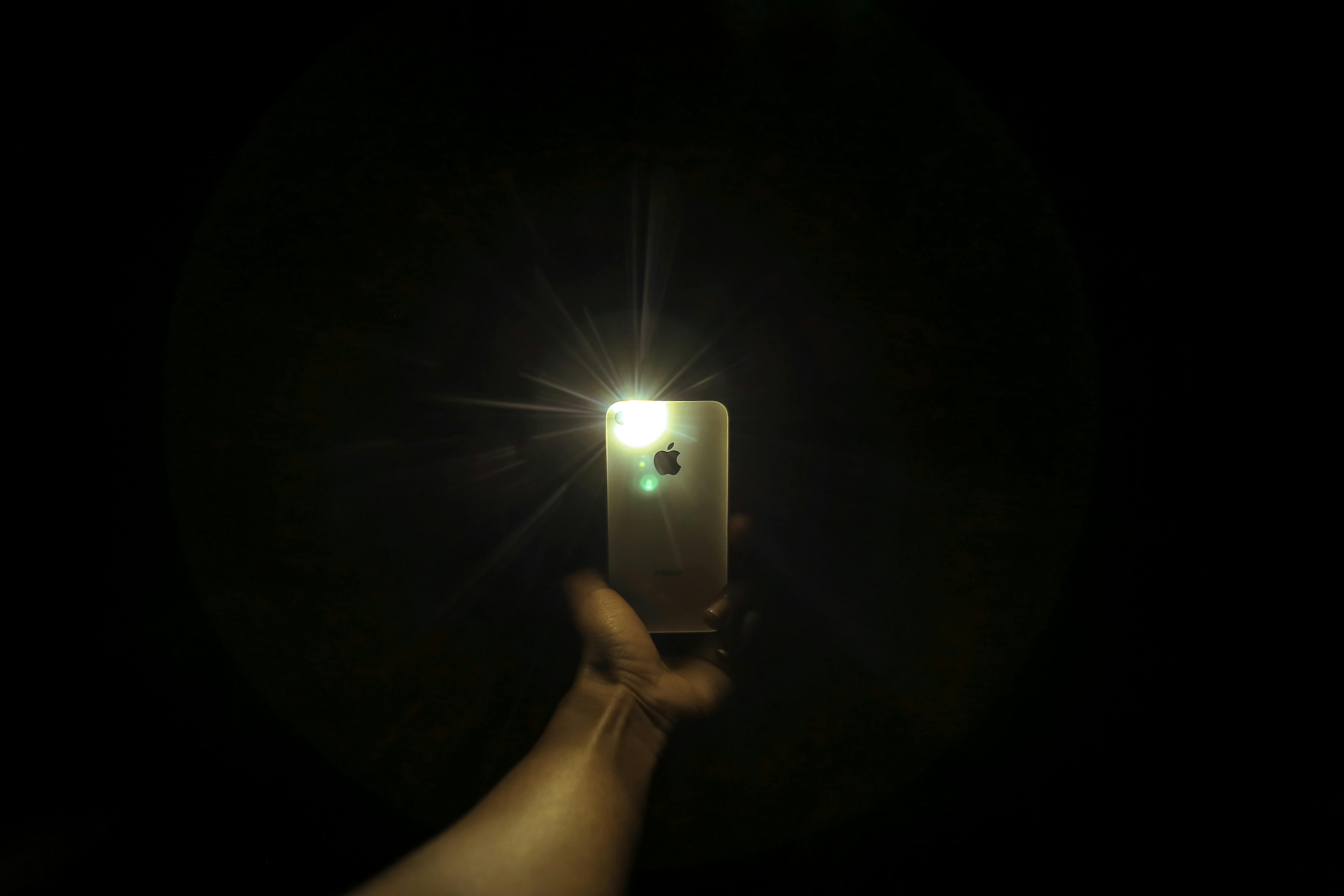 Smartphone flashlight illuminating a dark room to find hidden cameras during detection sweep.