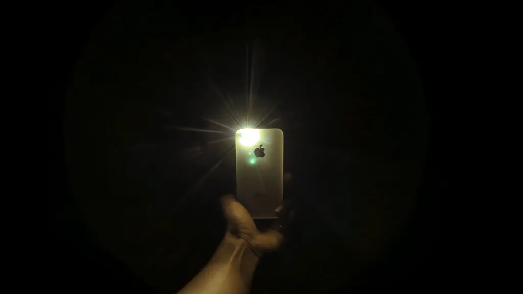 Person holding a smartphone with its light on in a dark room