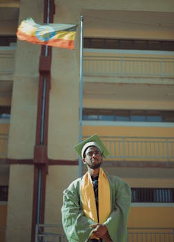 一名毕业生身着绿色礼服和帽子，骄傲地站在附近的旗帜旁