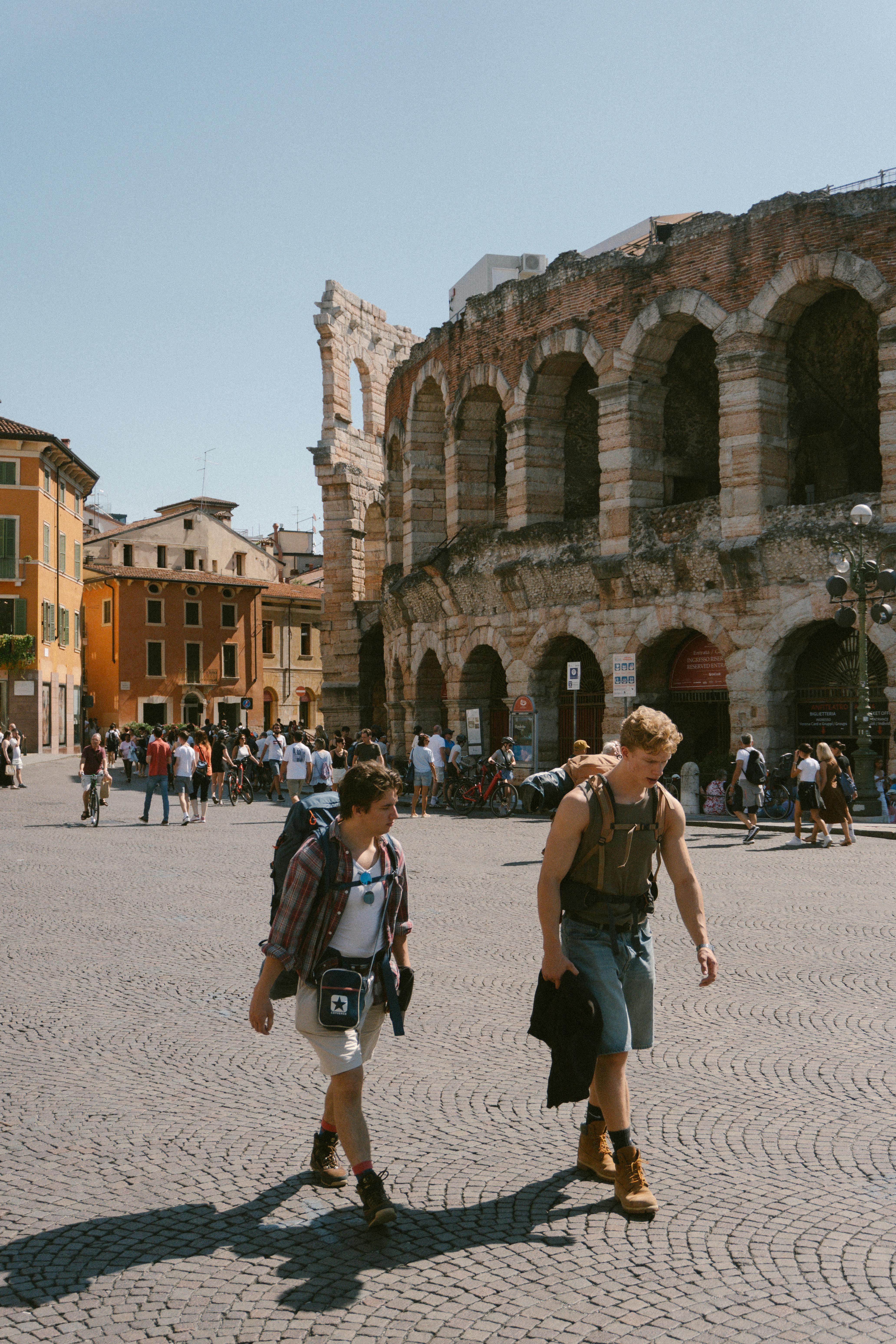 Ücretsiz Sıcak gün ışığında tarihi Verona Arena'nın yakınında yürüyen gezginler, İtalyan mimarisinin özünü yakalıyor. Stok Fotoğraflar