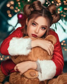 一位美丽的女人穿着红色圣诞老人服装，在模糊的圣诞灯光下拥抱一只泰迪熊