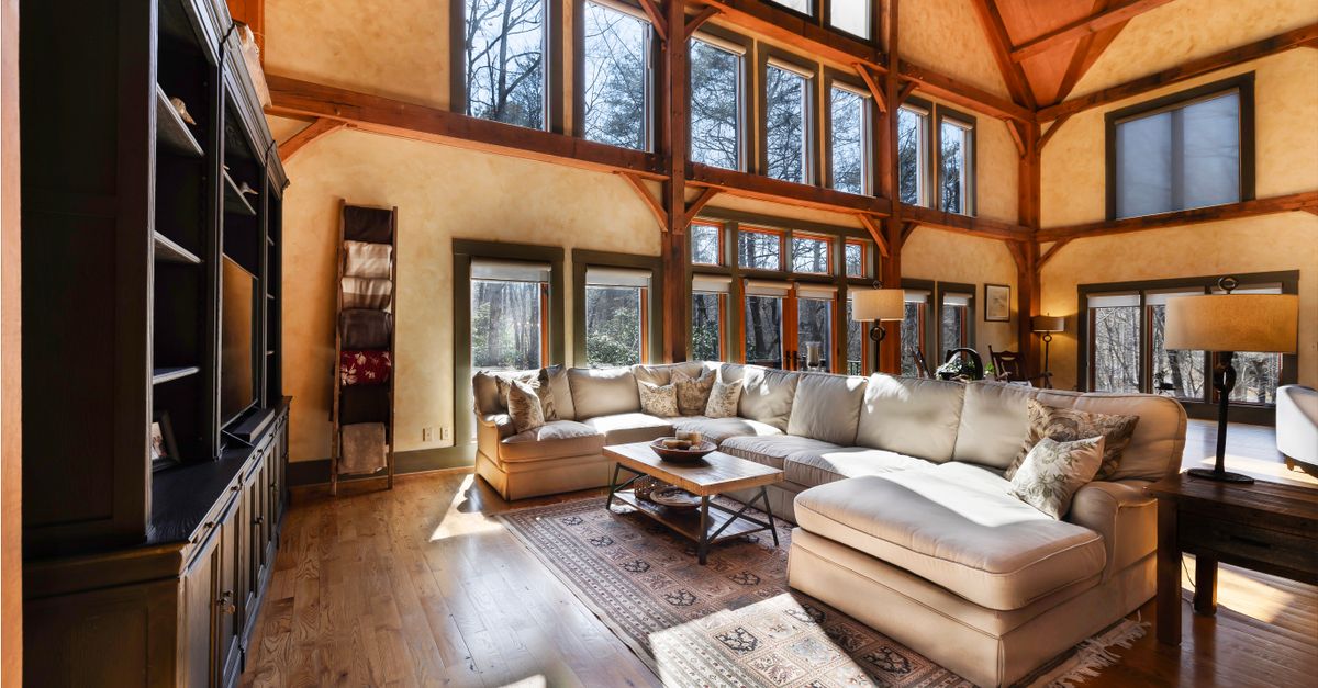 Bright rustic living room featuring large windows, a cozy sofa, and wooden beams.