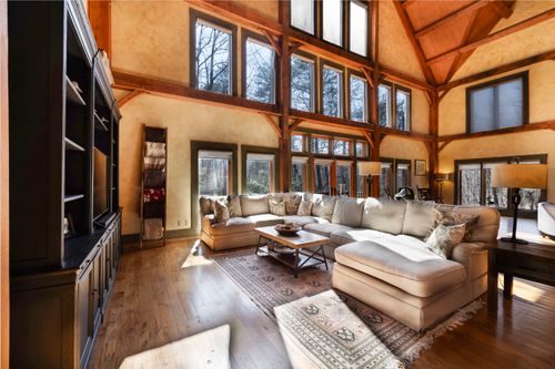Free Bright rustic living room featuring large windows, a cozy sofa, and wooden beams. Stock Photo