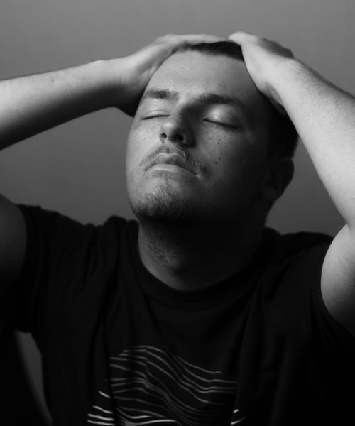Free Black and white portrait of an adult man with hands on head, eyes closed in contemplation. Stock Photo