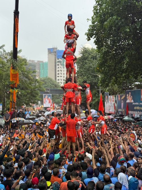 Free Crowd watching a vibrant human pyramid during festival celebration. Enthusiasm and teamwork on display. Stock Photo
