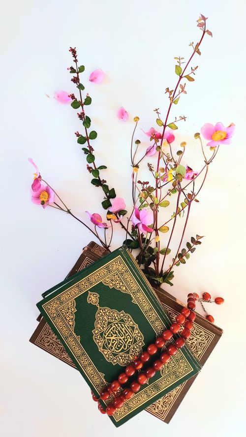 Free Flat lay of Quran, prayer beads, and pink flowers on a white background. Stock Photo