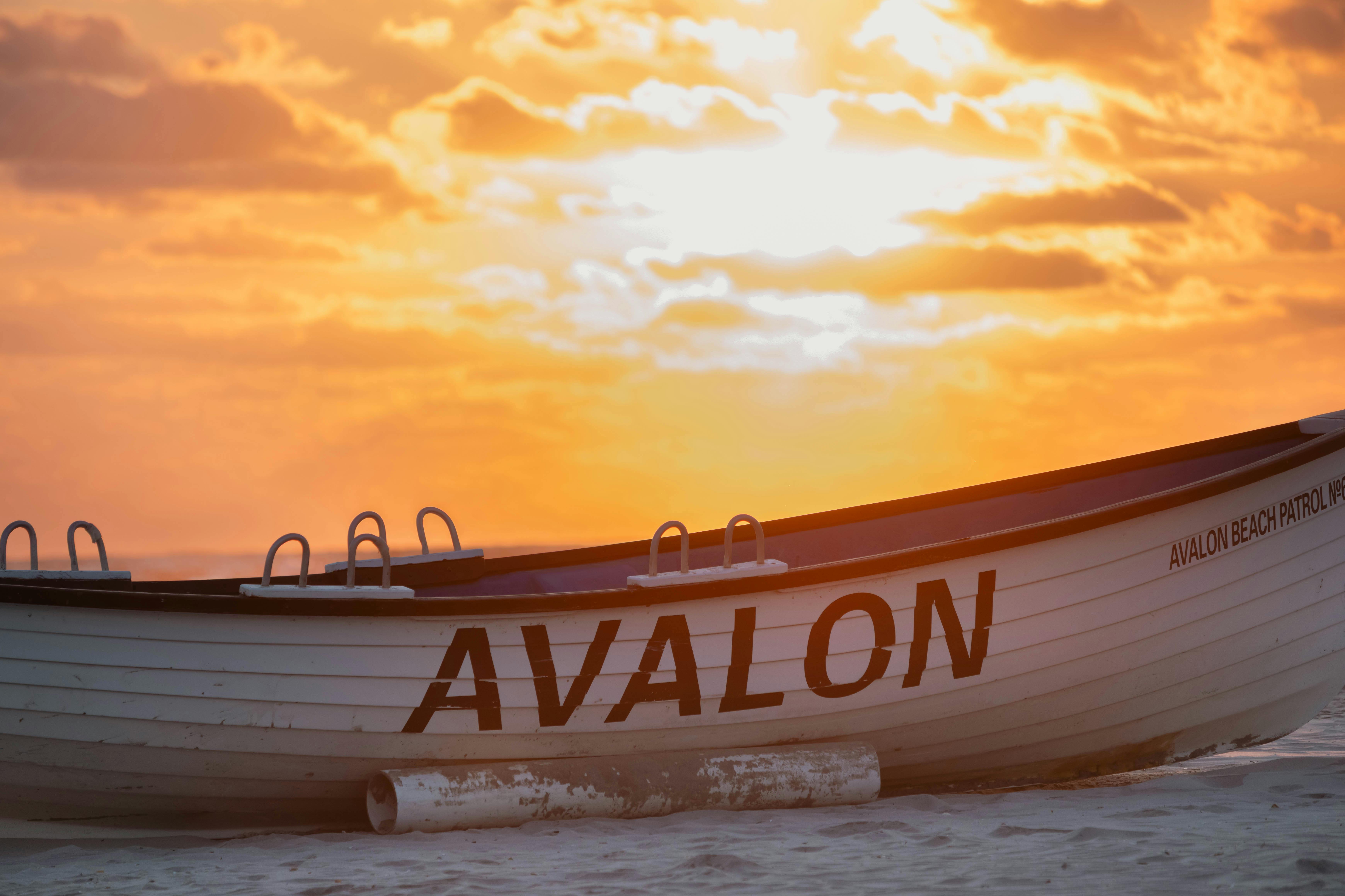 A lifeguard boat named Avalon rests on a sandy beach with a vibrant sunset in the background.