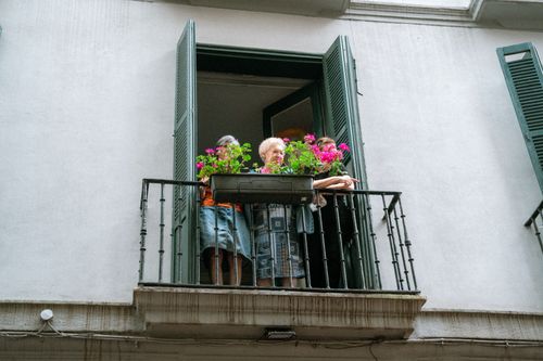 Free An elderly woman standing on a balcony adorned with vibrant flowers, enjoying the view outdoors. Stock Photo