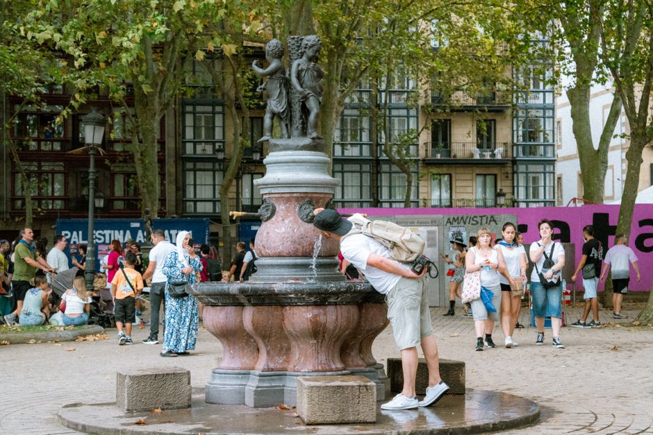Person refilling a reusable water bottle at a public fountain in Seville, Spain
