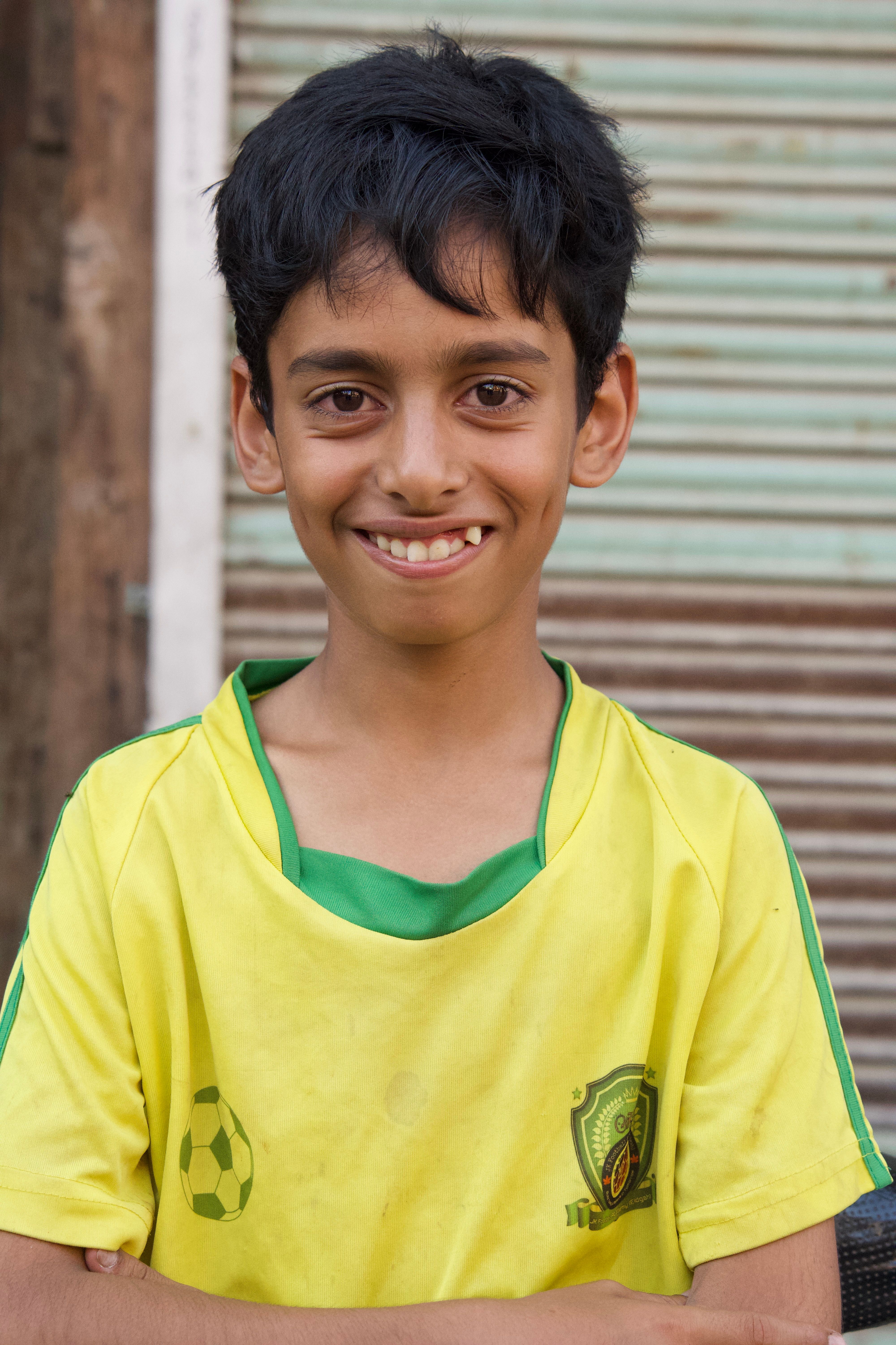 A cheerful boy posing in a yellow soccer jersey against a rustic backdrop.