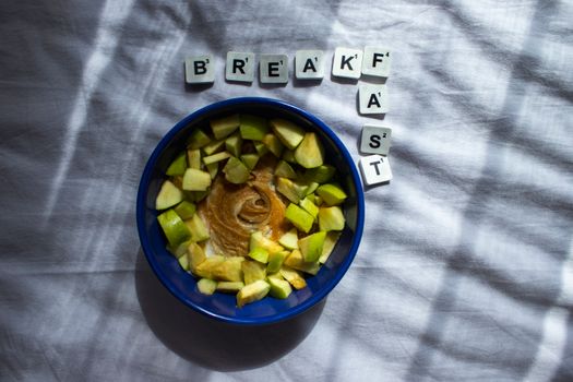 Overhead view of a breakfast bowl with peanut butter, apple, and banana, on a white background.