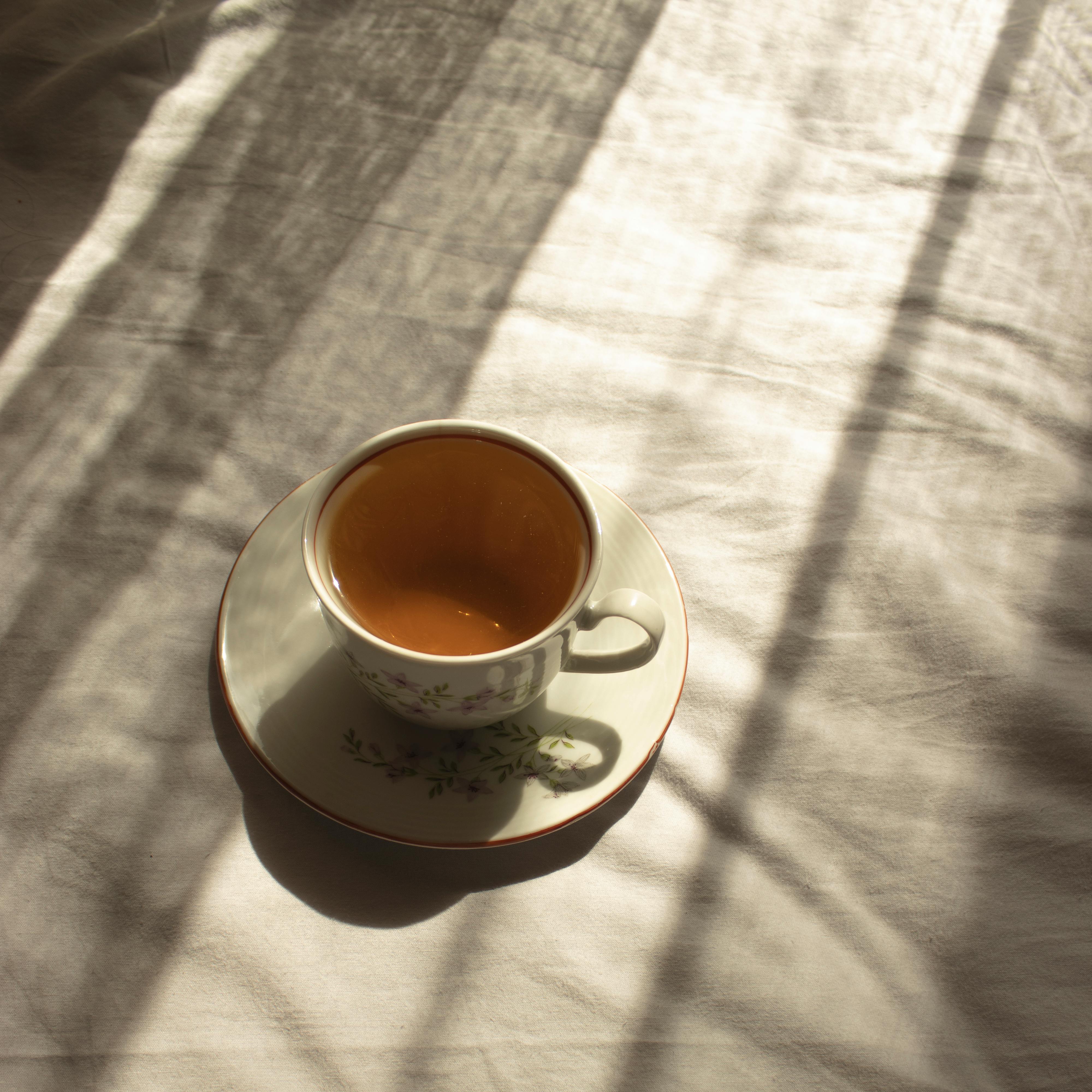A vintage teacup casts shadows on a sunlit fabric, creating a warm and nostalgic ambiance.
