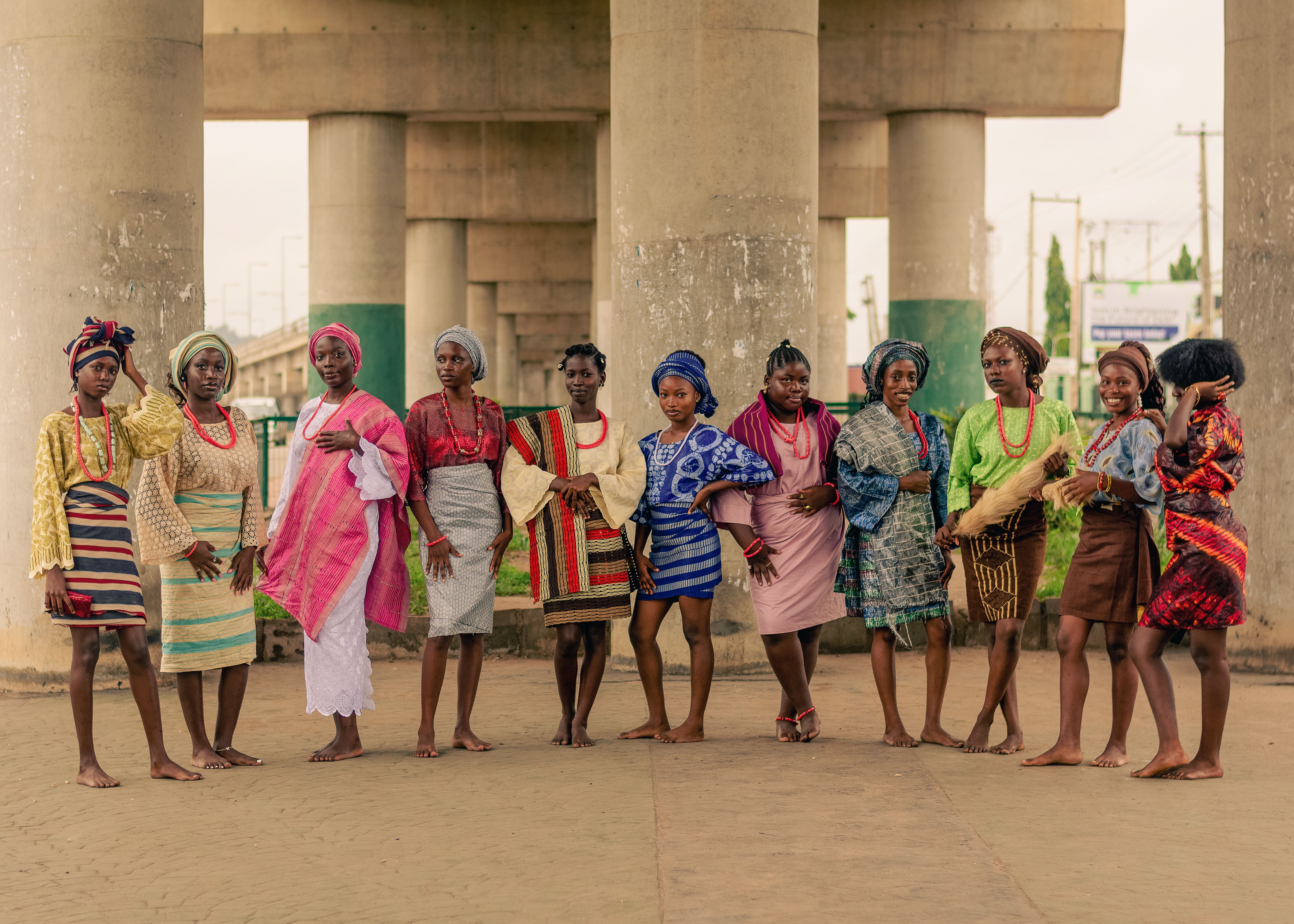 A group of women in vibrant traditional African attire pose under a bridge.