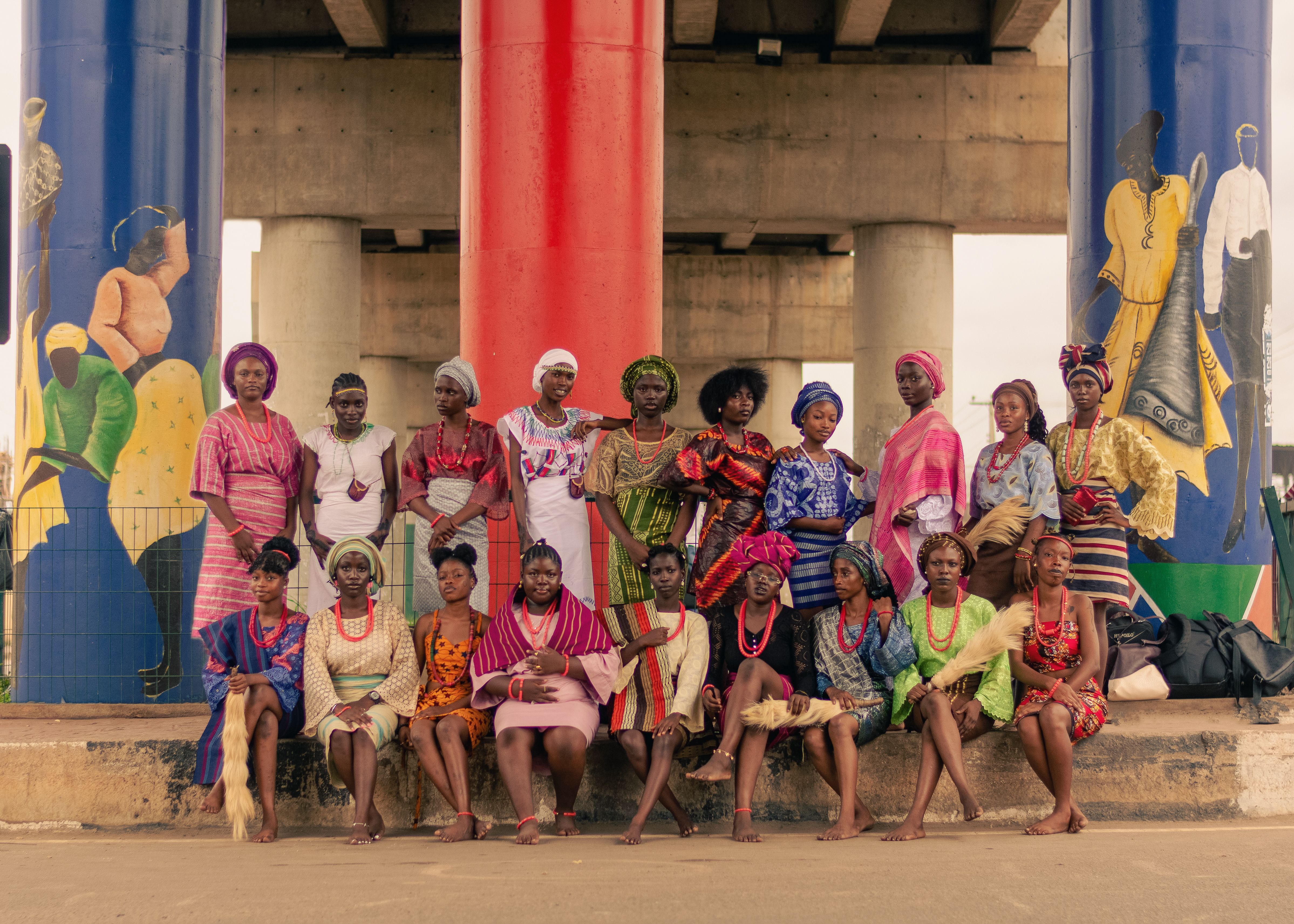 A group of women in vibrant traditional clothing poses under a decorated overpass.
