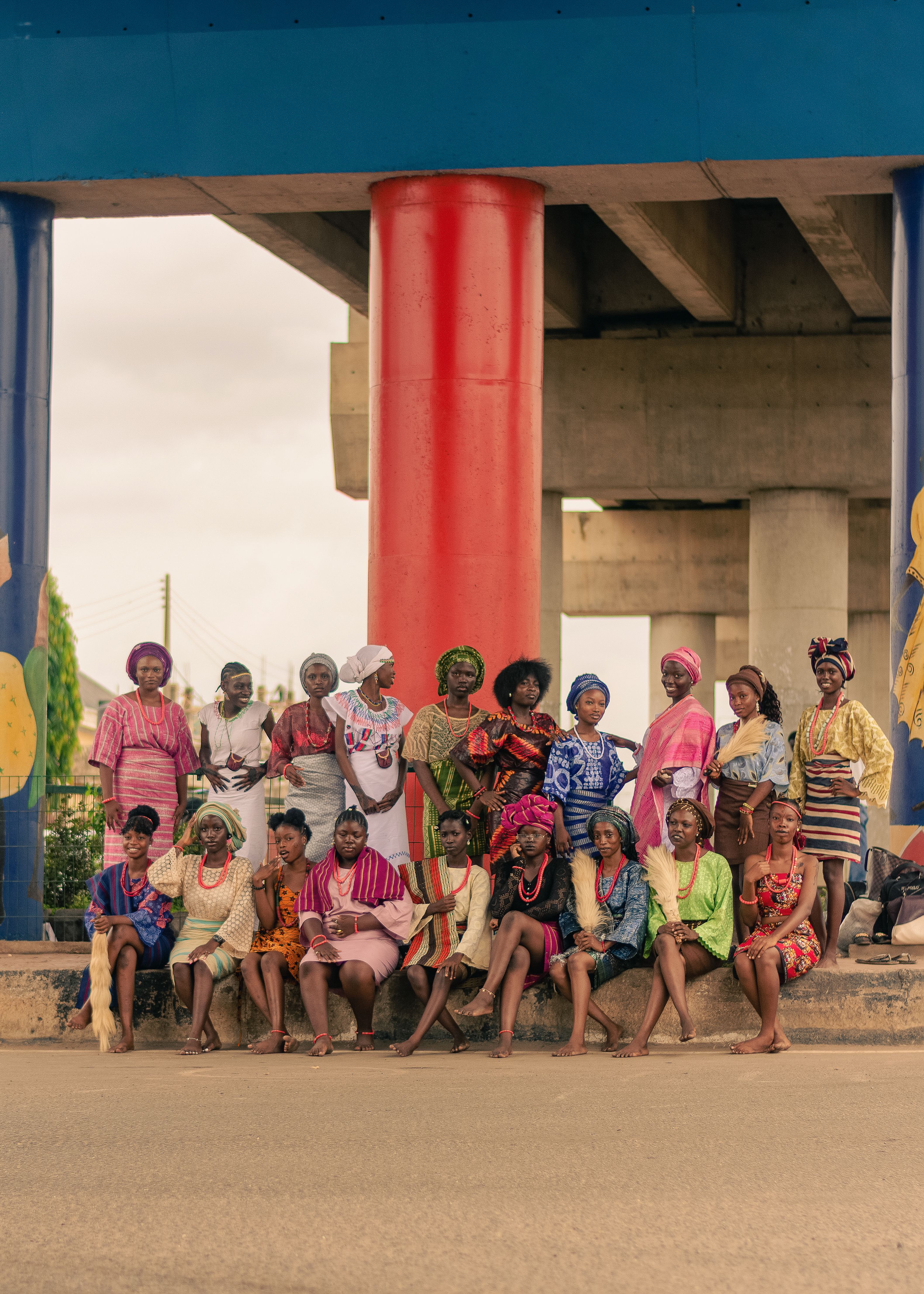 A diverse group of women in colorful traditional clothing outdoors under a bridge.