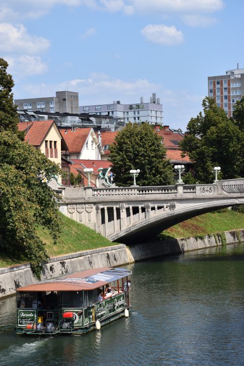 Free View of the Dragon Bridge in Ljubljana with scenic city architecture and canal boat. Stock Photo