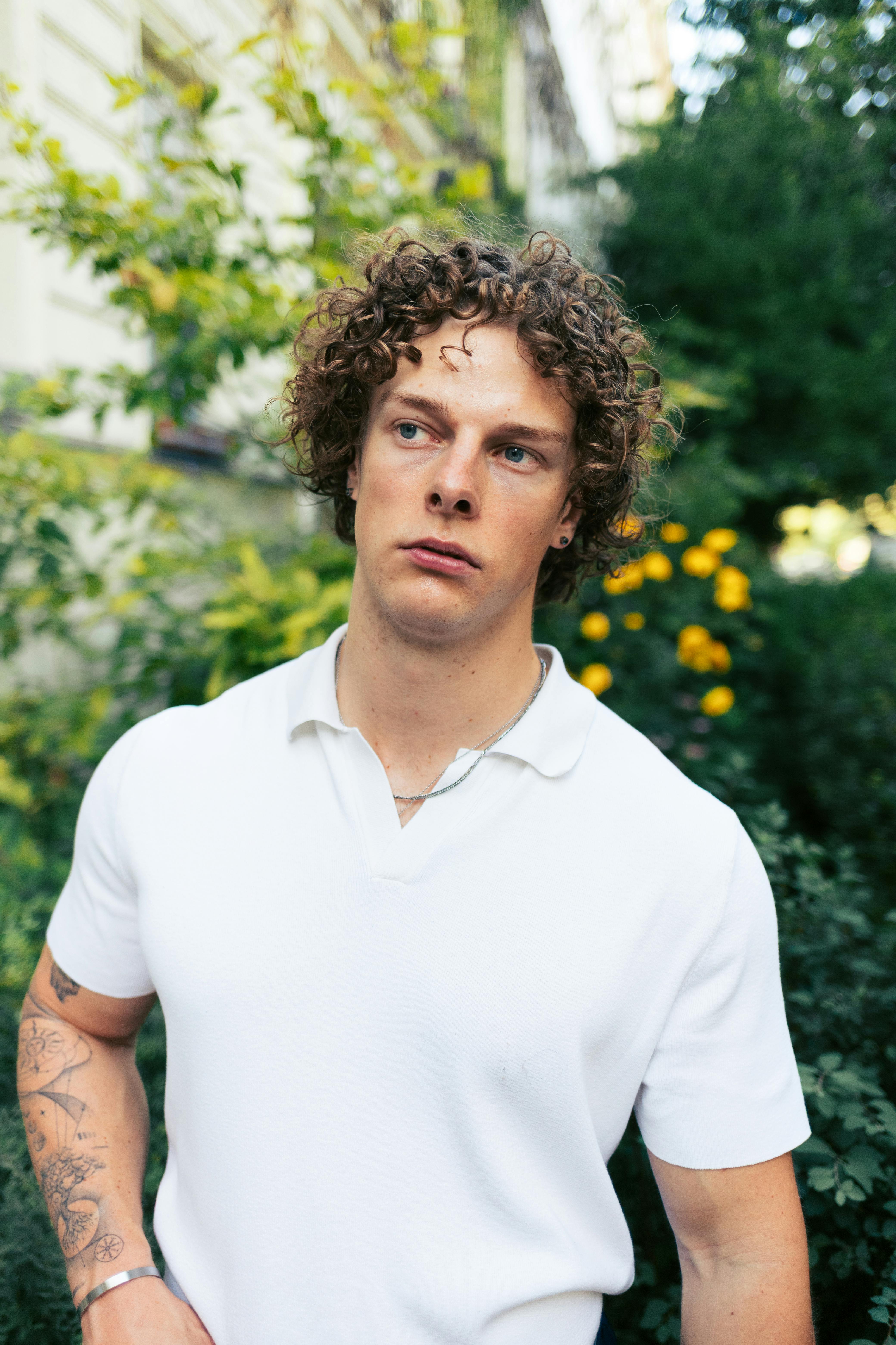 Casual outdoor portrait of a young man in a Berlin garden with greenery backdrop.