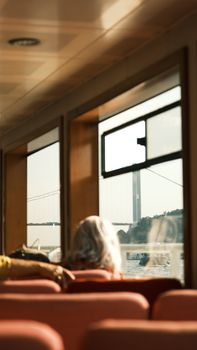 Elderly woman enjoys a scenic ferry ride with a view of a suspension bridge.