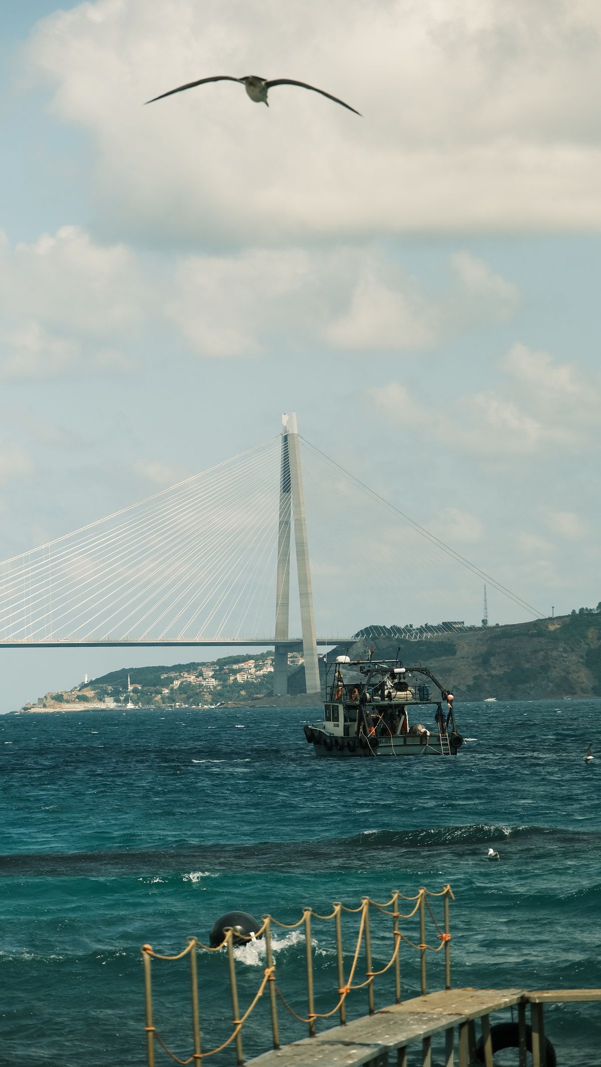A small fishing boat on the ocean with a suspension bridge in the background over the Seto Inland Sea