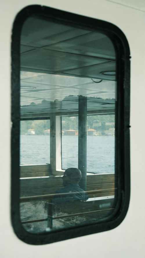 Free Elegant reflection of a passenger seen through a boat window with scenic lake view. Stock Photo