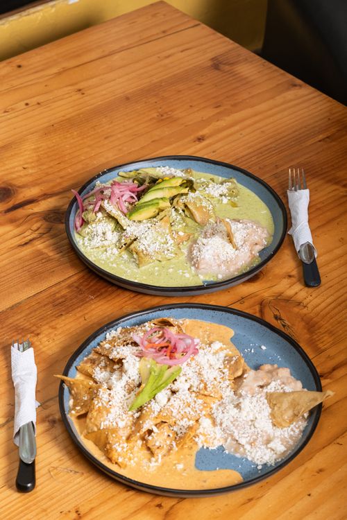 Free Two plates of chilaquiles topped with cheese, avocado, and pickled onions on a wooden table. Stock Photo