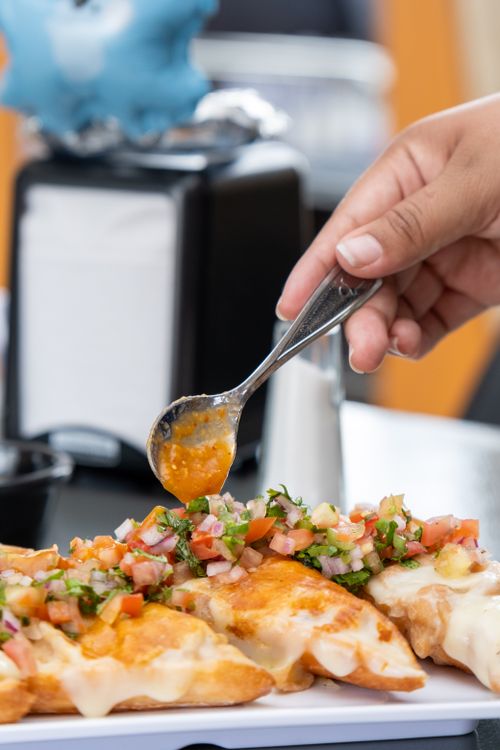 Free Hand spooning fresh salsa on cheesy quesadillas. Perfect culinary presentation showcasing vibrant Mexican flavors. Stock Photo