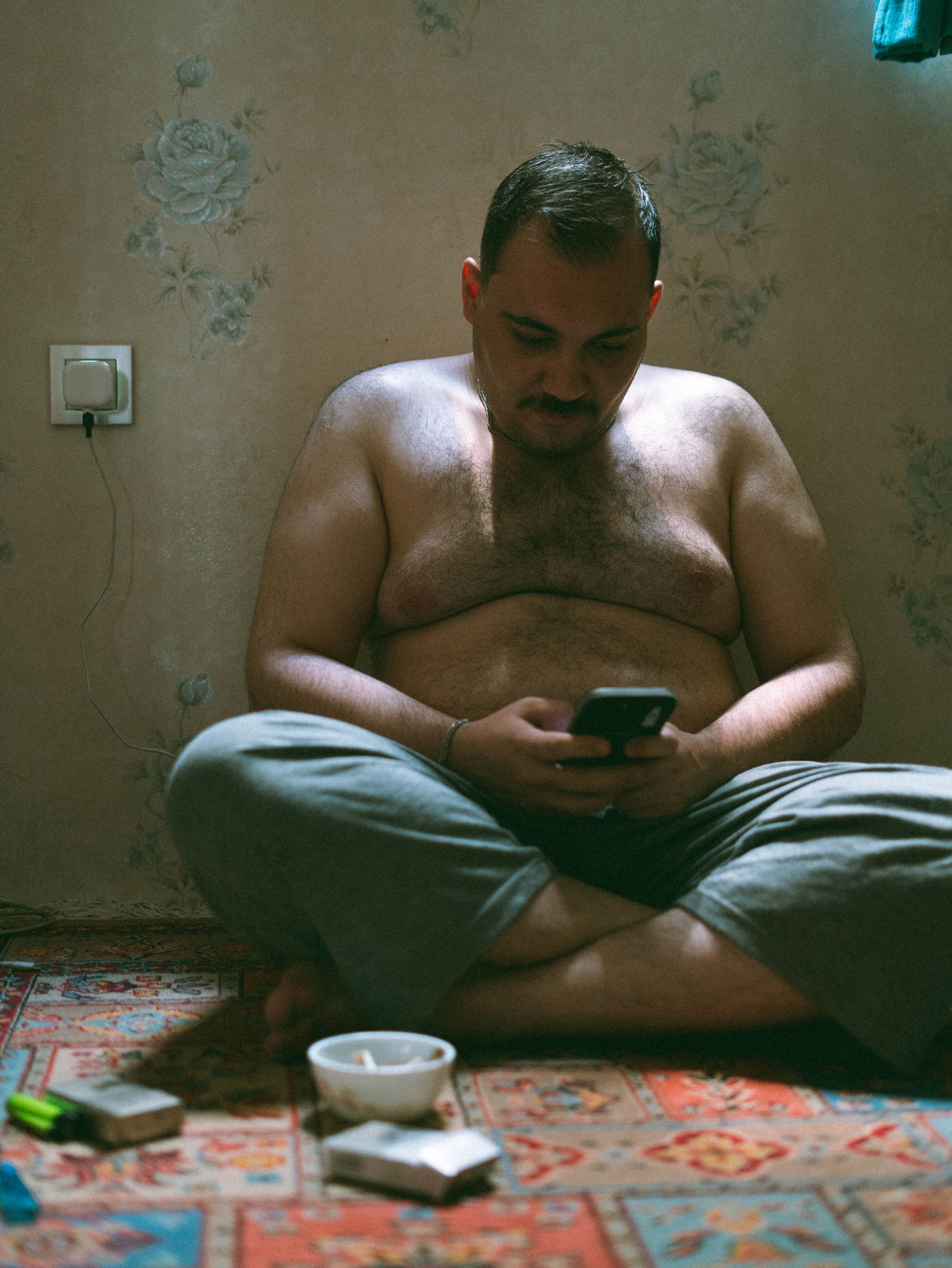 Man sitting on a rug indoors, focused on his smartphone, creating a casual and relaxed atmosphere.