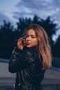 黄昏时分，一位时尚的年轻女子身着黑色皮夹克在户外摆姿势，散发出自信
