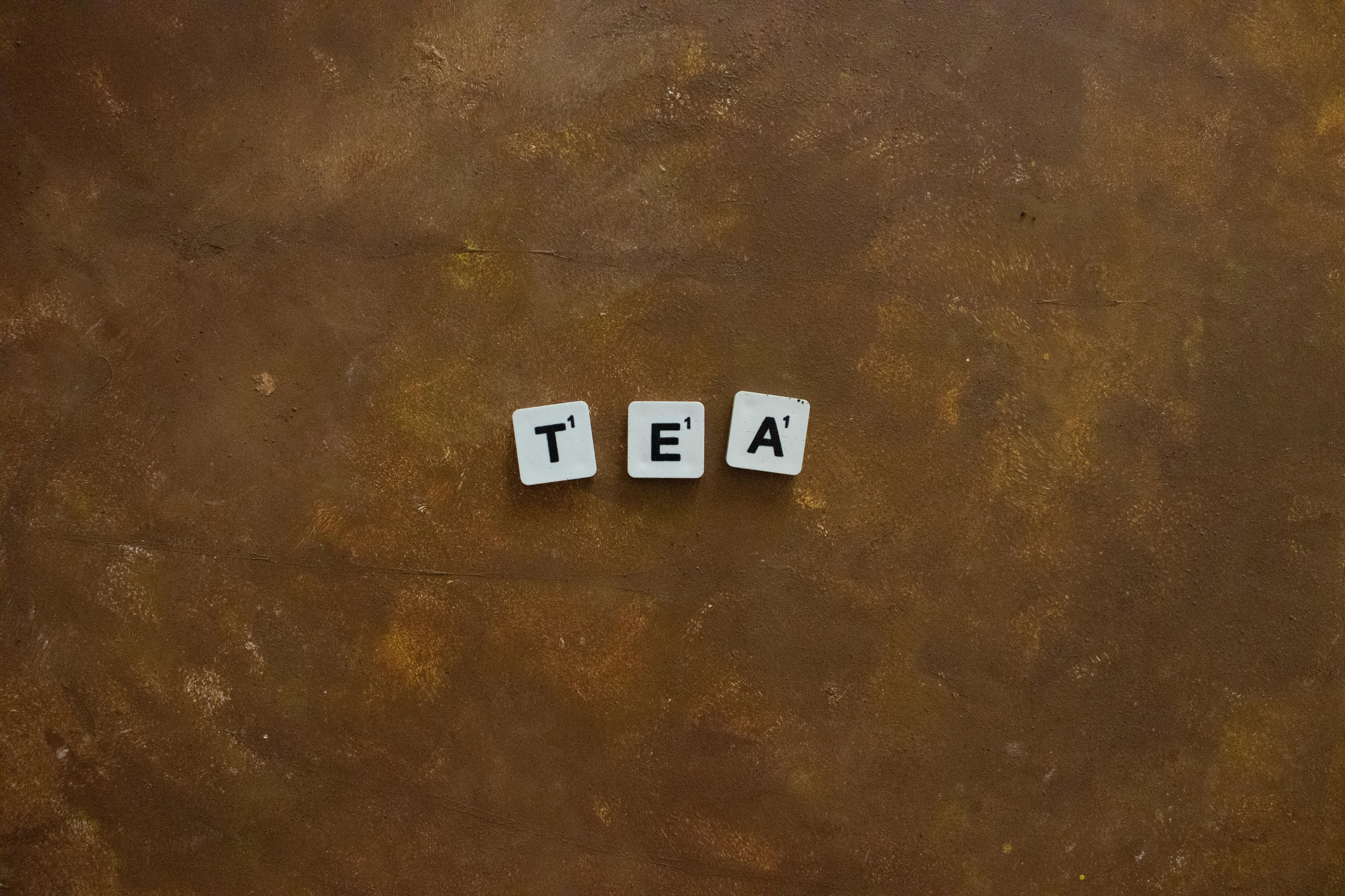 Scrabble tiles spelling 'tea' on a textured, warm-toned background. Perfect for words or tea themes.