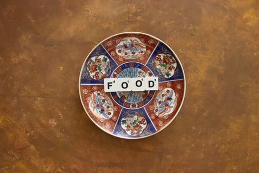 An overhead view of a decorative plate with Scrabble letters spelling 'Food' on a rustic surface.
