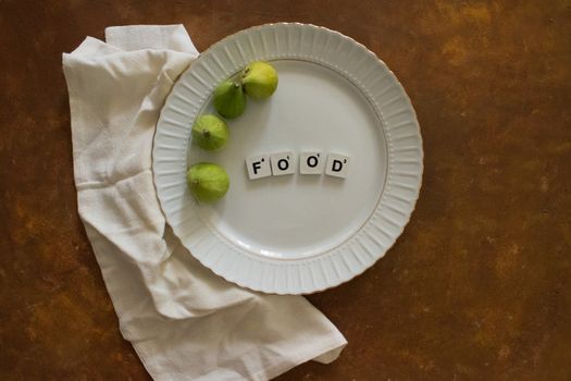 Top view of a white plate with figs and arranged food text on a rustic surface.