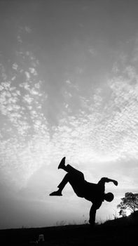 Silhouette of a breakdancer in mid-air against a dramatic sky.