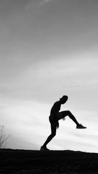 Silhouette of an athlete performing a high kick against a dramatic sky.