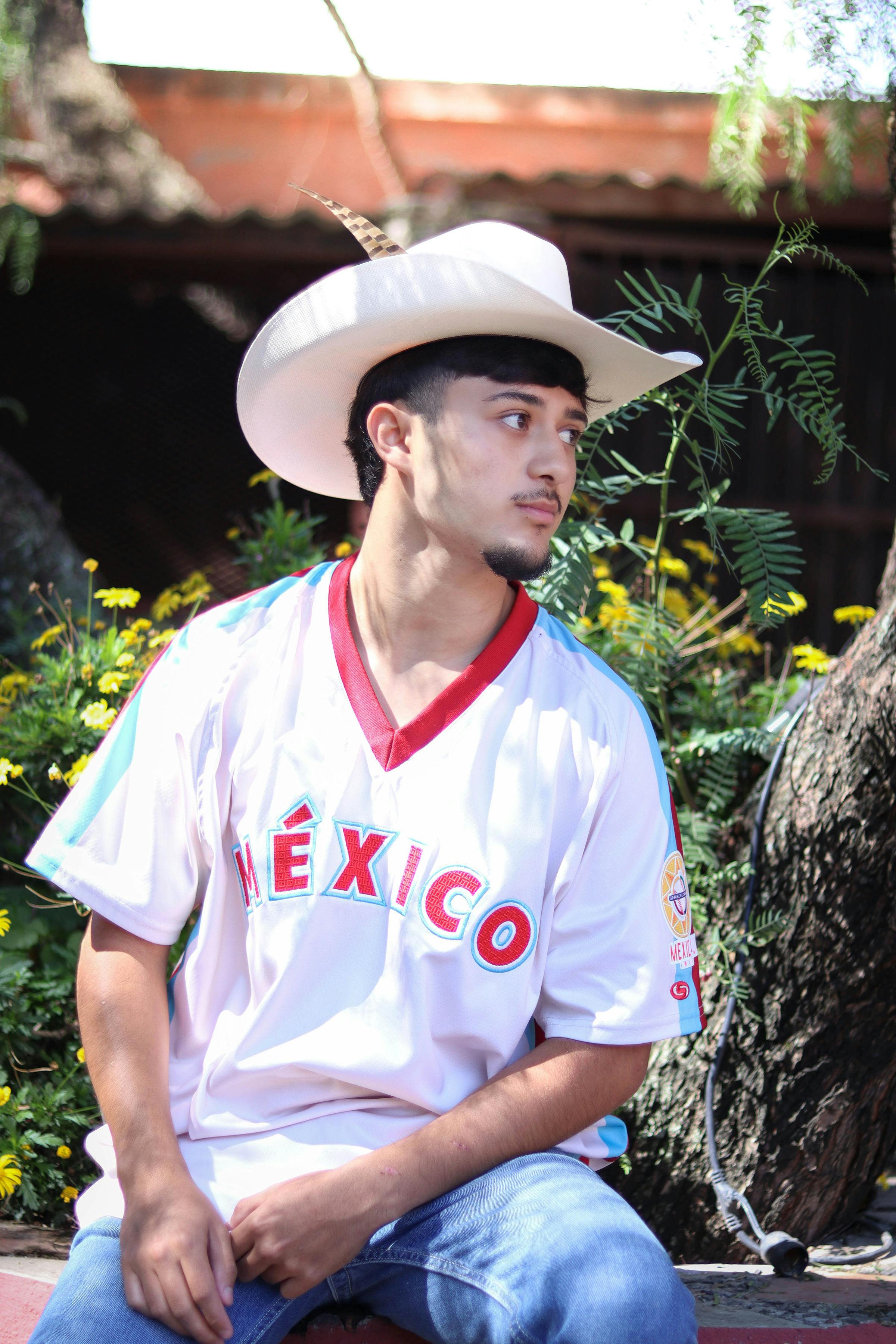 Young man in a Mexico jersey and cowboy hat sitting outdoors in León, Mexico.
