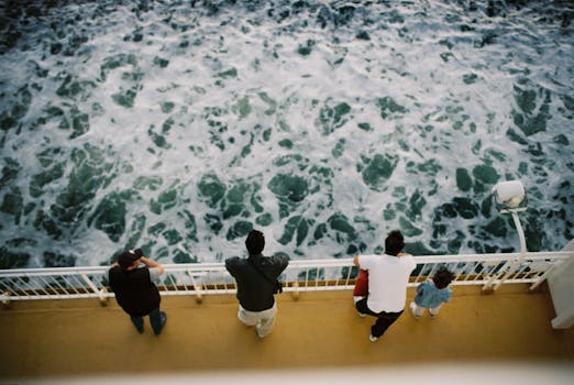 People watching ocean waves from ferry rail on a sunny day.