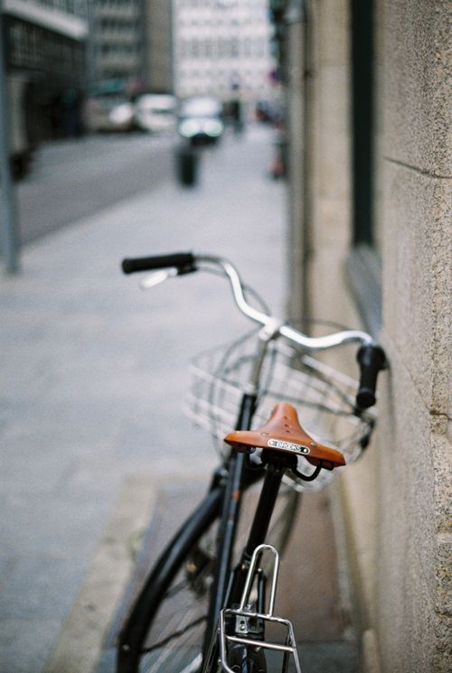 Free Close-up of a vintage bicycle with brown leather seat parked on a stone street in an urban setting. Stock Photo