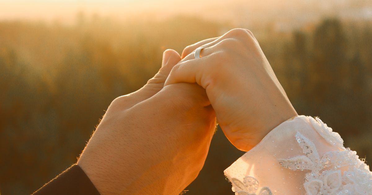 Two hands clasped together in warm golden sunset light with a wedding ring, symbolizing the commitment and relationship timing behind a Destiny Matrix marriage reading