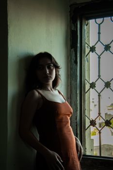 A moody portrait of a woman in a dimly lit room by a vintage window.