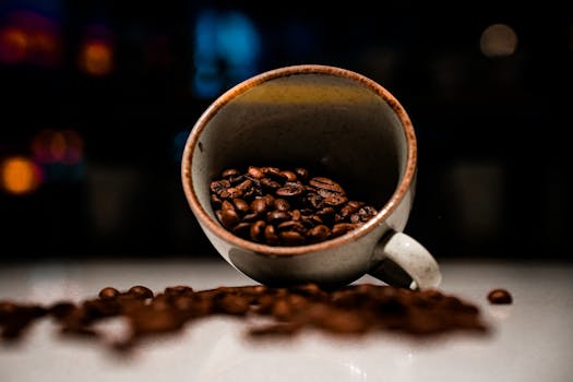 Close-up of coffee beans spilling from a rustic ceramic mug in a dark setting.