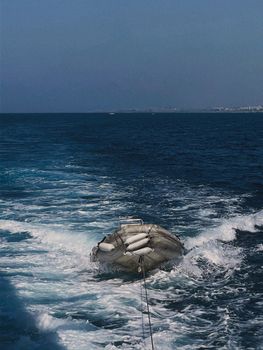 An inflatable rescue raft attached to a boat floating in a vast blue sea during a bright day.