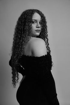 Stylish portrait of an elegant woman in a black dress with curly hair looking over her shoulder.