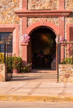 Stone building entrance with colorful flowers and sunlight in Acapulco, México.