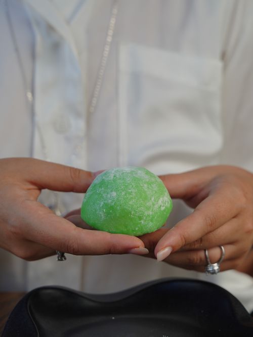 Free A close-up of hands gently holding a green mochi dessert over a black plate, indoors. Stock Photo