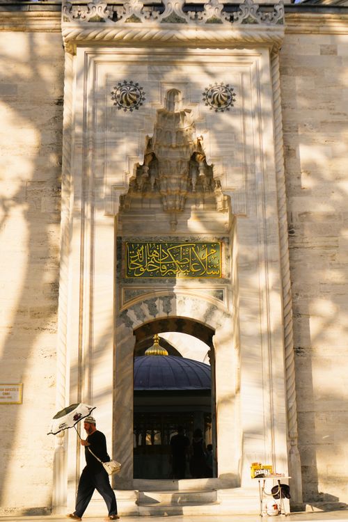 Free Man walks past an ornate, sunlit architectural entrance with intricate carvings and Arabic calligraphy. Stock Photo